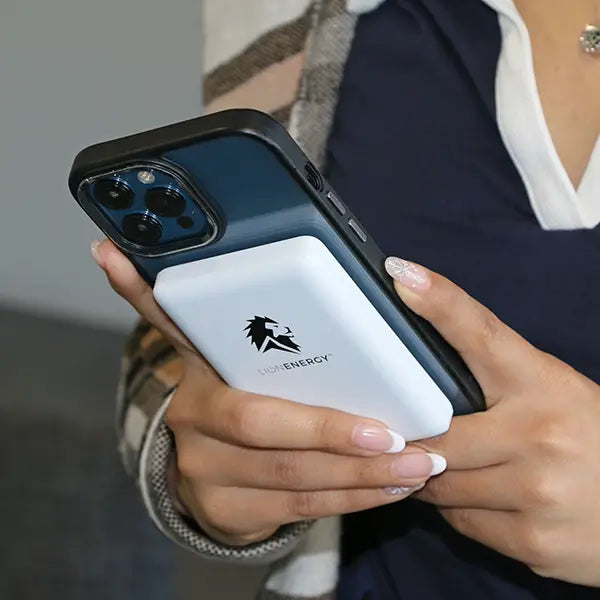 A person holding a smartphone with a white magnetic Lion Claw power bank from Lion Energy Staging attached to the back, featuring a lion logo.