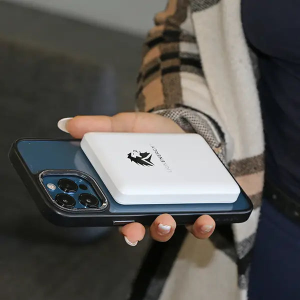 A person holds a smartphone with the Lion Claw magnetic power bank by Lion Energy Staging attached to its back, providing convenient battery backup on the go.