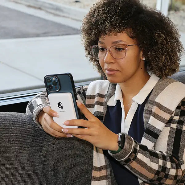 A curly-haired person with glasses sits on a couch, using their smartphone as the Lion Energy Staging Lion Claw magnetic power bank keeps it charged.